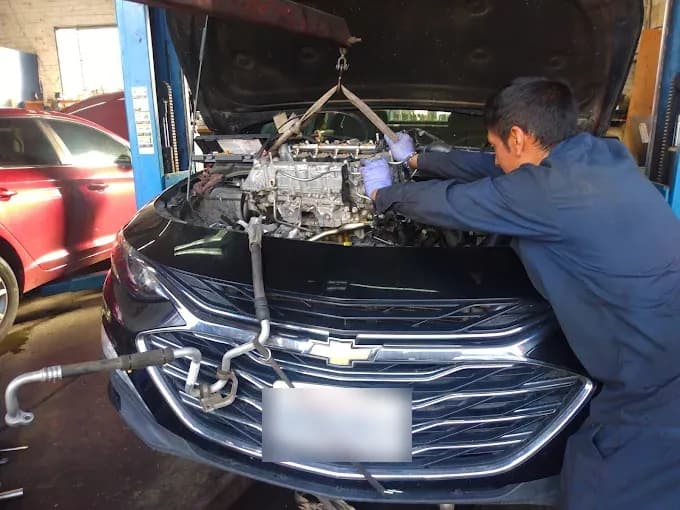 A mechanic lowering an engine into a Chevy on the lift